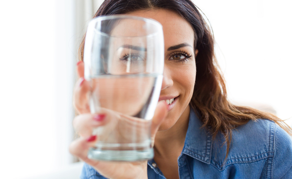 pretty-young-woman-smiling-while-looking-at-the-camera-through-the-glass-of-water-at-home-
