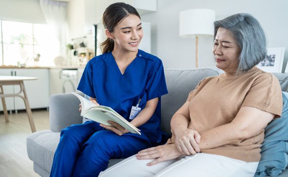 asian-woman-nurse-taking-care-of-senior-elderly-female-at-nursing-home-young-caregiver-therapist-doctor-sit-on-sofa-read-a-book-to-happy-older-handicapped-patient-medical-insurance-service-concept-
