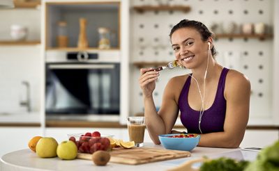 young-happy-athletic-woman-eating-fruit-salad-in-the-kitchen-