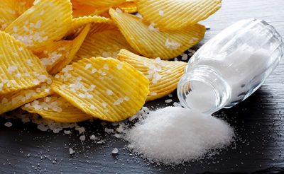 Batatas fritas com sal, ao lado de uma garrafa de sal derramada numa mesa de madeira. O consumo excessivo de sal pode levar à diabetes tipo 2. 