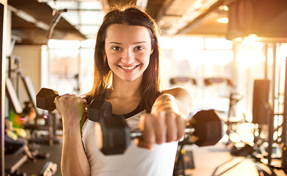 Uma jovem mulher a usar pesos de mão num ginásio para fortalecer os músculos.