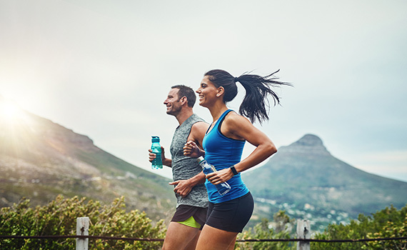Um homem e uma mulher a correr, cada um com uma garrafa de água na mão para se reidratarem após o exercício. 