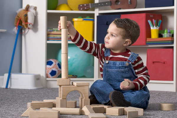 boy-building-with--looking-at-tall-wooden-toy-blocks-horizontal