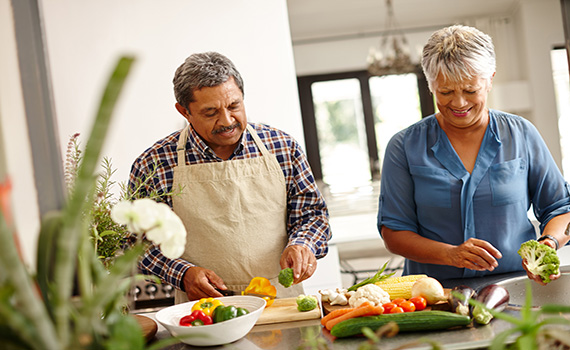 Duas pessoas idosas a preparar comida saudável. 