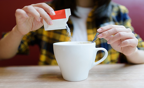 Uma mulher adulta deita açúcar na sua chávena de café. 