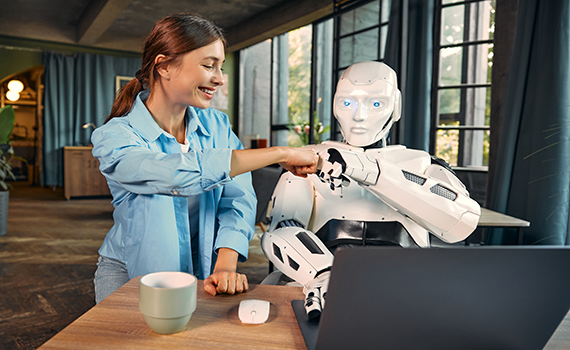 Um robô com uma mulher a trabalhar num computador num escritório. 
