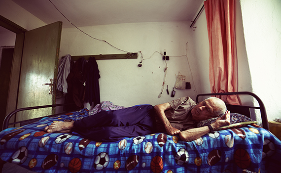 Um adulto idoso deitado na cama com um ar triste e solitário. 