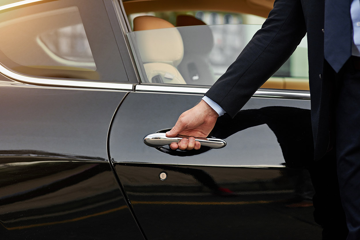 Um homem abre a porta do passageiro de seu carro de luxo. 