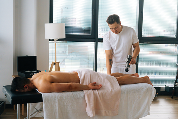 Um atleta profissional a receber massagem terapêutica com o dispositivo portátil de massagem de percussão num salão de beleza. 