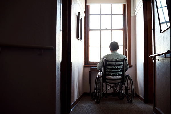 Um adulto idoso sentado numa cadeira de rodas a olhar pela janela.