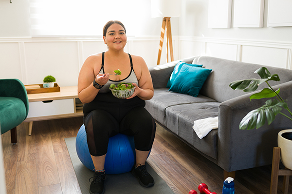 Uma mulher com excesso de peso come uma salada depois do treino. 