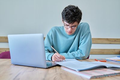 Um jovem estudante a assistir às suas aulas em linha e a tomar notas pessoais no seu caderno.  