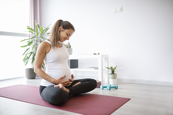 Uma mulher grávida está a fazer ioga em casa para gerir o stress. 