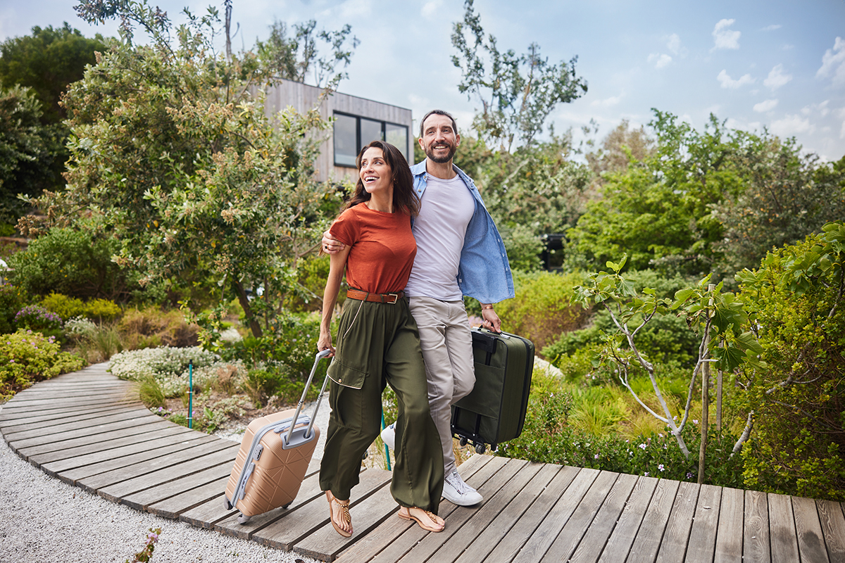 Um casal caminha com suas malas para uma casa que alugou pelo aplicativo do Airbnb