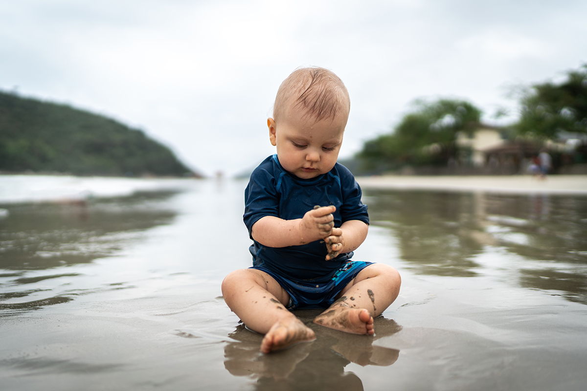 Um bebê brinca com areia molhada em uma praia. 