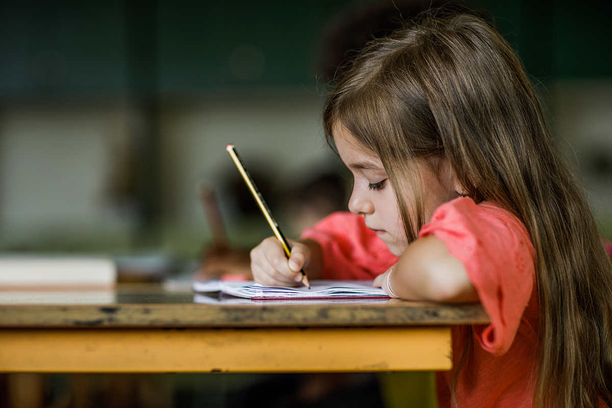 Menina escrevendo em um caderno. 