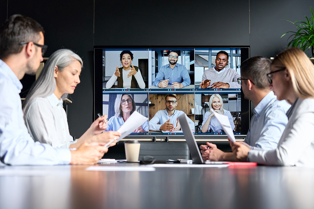 Videoconferência on-line de uma corporação global em uma sala de reuniões com diversas pessoas sentadas em um escritório moderno e colegas multiétnicos e multiculturais em um monitor de tela grande. 