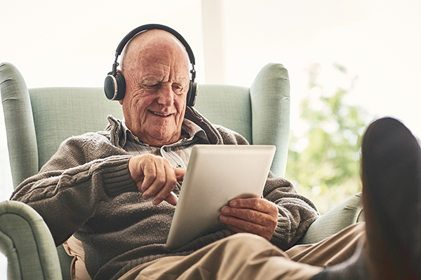 Um adulto mais velho utiliza um tablet e auscultadores para comunicar com a família e os amigos. 