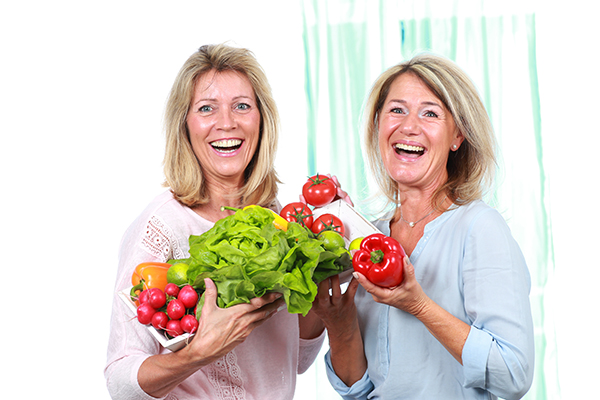 Duas mulheres adultas seguram alegremente legumes nas mãos.