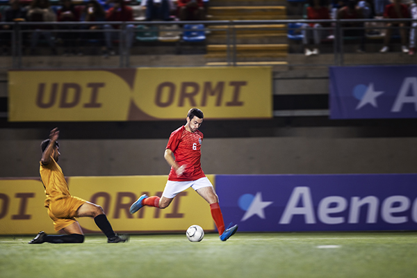 Jogadores de futebol num estádio com uma multidão ao fundo. 