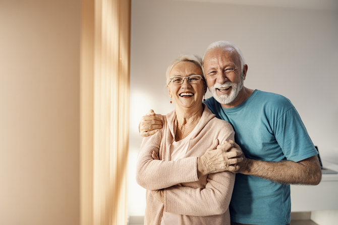 senior-couple-hugging-in-a-nursing-home-a-happy-senior-couple-standing-next-to-a-window-in-a-nursing-home-hugging-and-smiling-they-have-all-care-they-need-