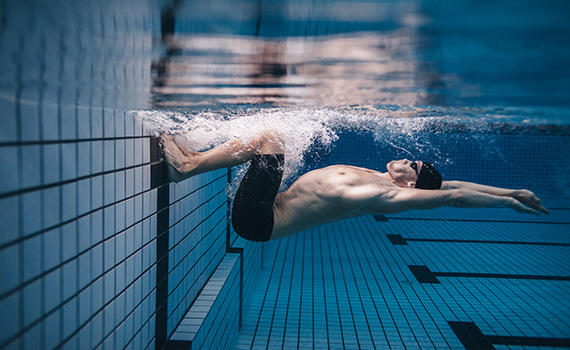 Un hombre joven con condiciones crónicas realizando entrenamiento acuático intervalado de alta intensidad en una piscina para mejorar su capacidad física. 