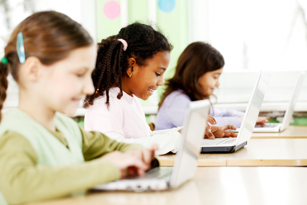 Tres alumnas sonriendo mientras usan ordenadores portátiles en el aula