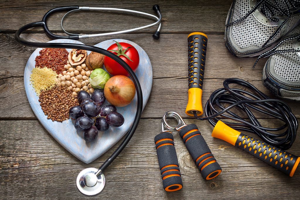Concepto de una vida saludable. Una plato con forma de corazón con diferentes frutas adentro. Al lado, accesorios para hacer ejercicio. 