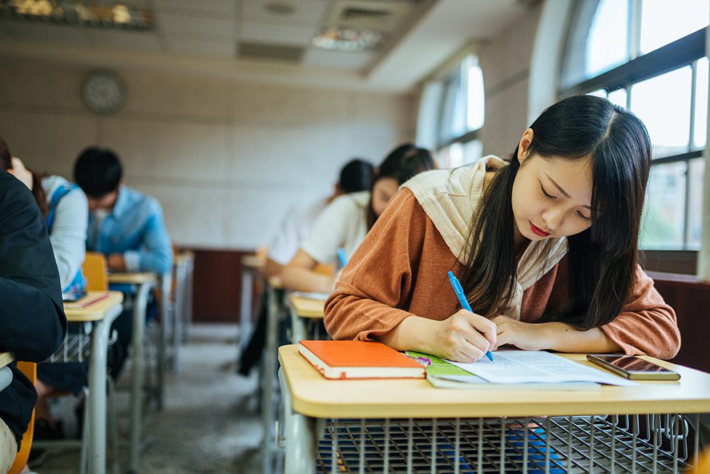 Mujer asiática realizando un examen en un salón de clases. 