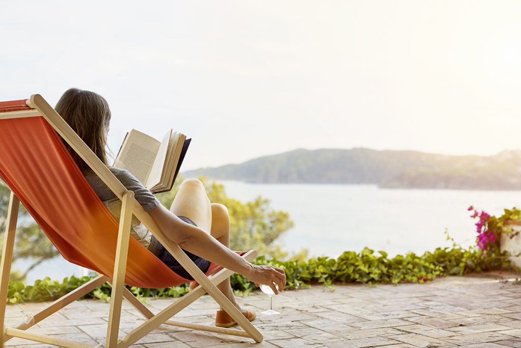 Beneficios del descanso. Mujer leyendo un libro mientras se relaja en una tumbona en el patio trasero.